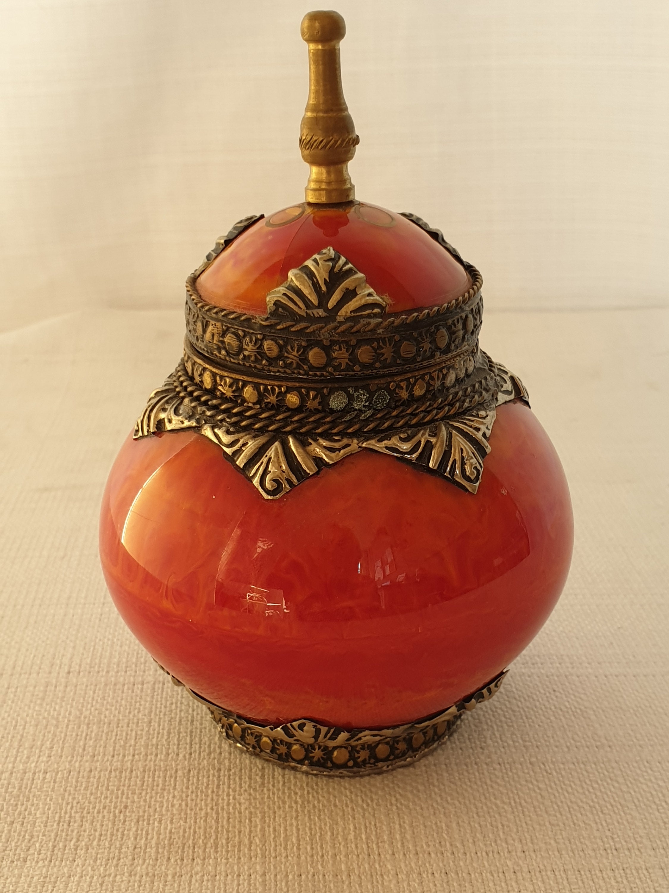Two ornate orange lid jars, finished with brass ornaments.