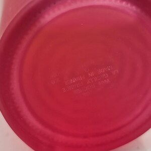 May include: Close-up of the base of a red glass bottle. The circular base has a slightly textured surface. Text on the base reads "Yves Rocher, La Gacilly France, Made in France, 201".