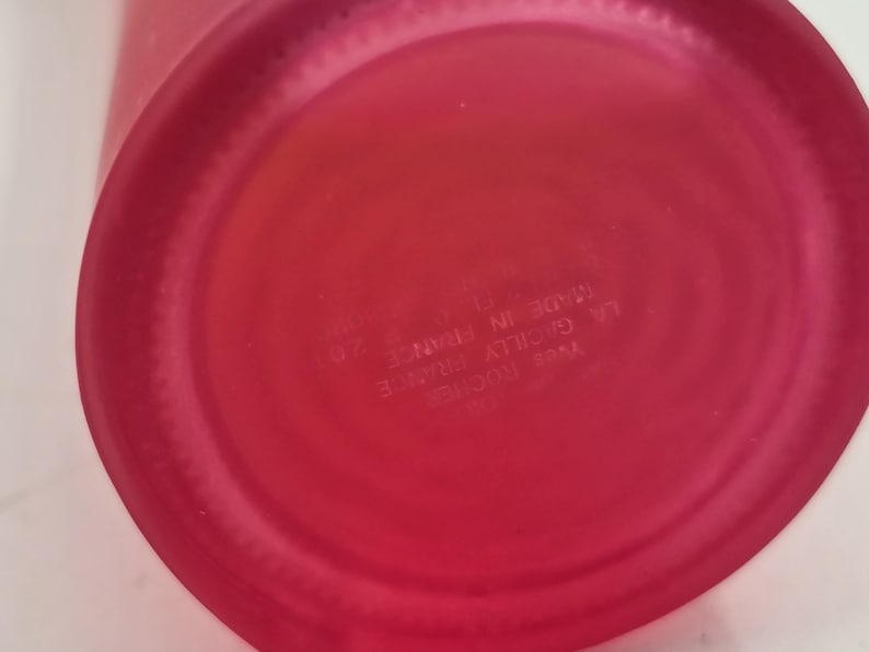 May include: Close-up of the base of a red glass bottle. The circular base has a slightly textured surface. Text on the base reads "Yves Rocher, La Gacilly France, Made in France, 201".