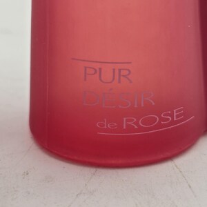 May include: A close-up of a red bottle with the words "PUR D&Eacute;SIR de ROSE" printed in a lighter color. The bottle has a smooth, matte finish and a slightly curved shape. The text is centered on the bottle.