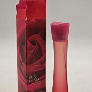 May include: A red and pink perfume bottle and box. The box displays a close-up of a red rose and the text "PUR DESIR de ROSE". The bottle is a slender, curved shape with a pink cap. The box reads "eau de toilette vaporisateur spray". The bottle contains 60 ml.
