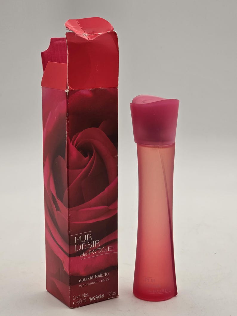 May include: A red and pink perfume bottle and box. The box displays a close-up of a red rose and the text "PUR DESIR de ROSE". The bottle is a slender, curved shape with a pink cap. The box reads "eau de toilette vaporisateur spray". The bottle contains 60 ml.