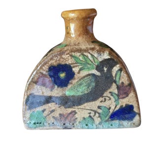 Può includere: Una piccola bottiglia in ceramica semicircolare con una finitura smaltata color marrone chiaro e screpolata. La superficie anteriore presenta un disegno dipinto a mano di un uccello scuro, foglie verdi e fiori blu e viola. Collo corto.