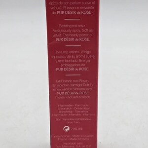 May include: A red rectangular box with text in multiple languages, including English, French, German, and Spanish. The text describes a fragrance called "PUR D&Eacute;SIR de ROSE" and includes the phrase "Budding red rose."