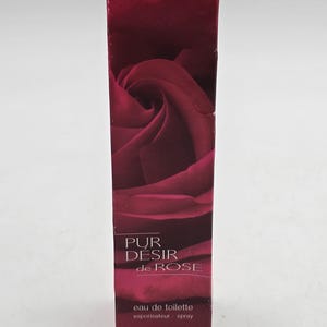 May include: A dark red rectangular box of "Pur D&eacute;sir de Rose" eau de toilette. The box features a rose image. The text "PUR D&Eacute;SIR de ROSE" is printed in white. The box contains 60 ml of eau de toilette.