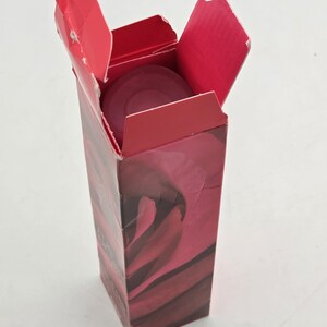 May include: A red cardboard box with an open lid, revealing a circular, dark red object inside. The box has a floral design in shades of red and burgundy. The box is on a white surface.