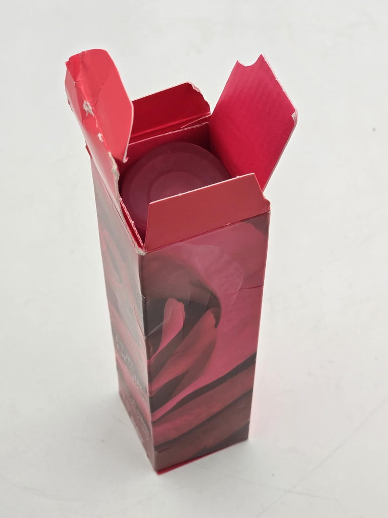 May include: A red cardboard box with an open lid, revealing a circular, dark red object inside. The box has a floral design in shades of red and burgundy. The box is on a white surface.