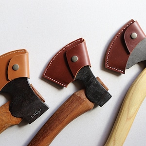 May include: Three leather-wrapped axes with wooden handles. The axes have black blades and brown leather sheaths with stitching and a button closure.