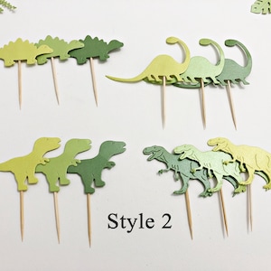 May include: A set of green dinosaur cupcake toppers. The toppers are made of cardstock and feature different dinosaur designs, including a stegosaurus, a brachiosaurus, and a tyrannosaurus rex. The toppers are perfect for adding a fun and festive touch to any dinosaur-themed party.