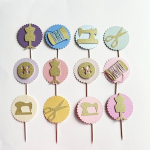 May include: A collection of twelve cupcake toppers with a sewing theme. Each topper features a gold glitter design on a scalloped circle. Designs include dress forms, spools of thread, sewing machines, buttons, and scissors. The toppers are on brown sticks.