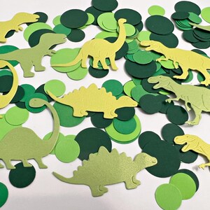 K&ouml;nnte beinhalten: Gr&uuml;ner und gelber Papier-Dinosaurier-Konfetti. Der Konfetti enth&auml;lt verschiedene Dinosaurierformen, darunter einen Stegosaurus, einen Brachiosaurus und einen Tyrannosaurus Rex.