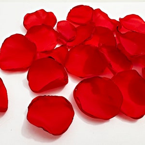 Może przedstawiać: Kolekcja żywych, czerwonych płatków róż rozrzuconych na białej powierzchni. Płatki mają głęboki, bogaty czerwony kolor z lekko błyszczącym wykończeniem. Te sztuczne płatki są idealne na wesela, imprezy lub inne cele dekoracyjne.