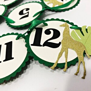 May include: Green and white paper circles with black numbers 9, 11, and 12. A gold glitter giraffe and a green leaf are attached to the circle with the number 12.