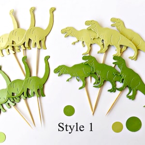 May include: A set of green and yellow dinosaur cake toppers. The toppers are made of paper and feature different types of dinosaurs, including a T-Rex and a Brontosaurus. The toppers are attached to wooden skewers. Style 1.