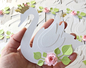 May include: White paper swan cutouts with a gold glitter crown and pink paper roses with green leaves.