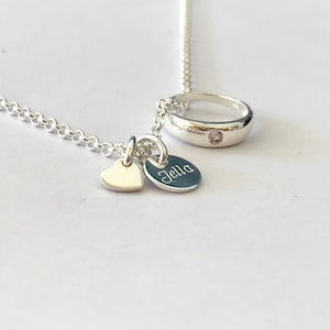 Könnte beinhalten: Silberne Halskette mit einem Ring-Anhänger, einem Herz-Anhänger und einem personalisierten Scheiben-Anhänger mit der Aufschrift "Jella".