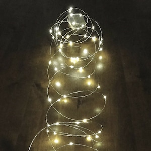 Könnte beinhalten: Eine Lichterkette mit warmweißen LED-Lichtern, die spiralförmig auf einer Holzoberfläche gewickelt ist.