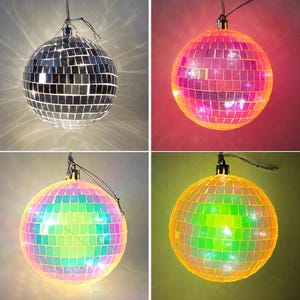 Könnte beinhalten: Ein Set aus vier kugelförmigen Discokugeln, die mit kleinen quadratischen Spiegelplättchen bedeckt sind. Eine Kugel ist silberfarben, während die anderen in leuchtendem Pink, Irisierend und Gelb strahlen, aufgehängt an einer schwarzen Schnur.
