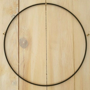 Könnte beinhalten: Ein schwarzer Metallring mit einem Durchmesser von etwa 30 cm. Der Ring hängt an einer hellbraunen Holzwand.