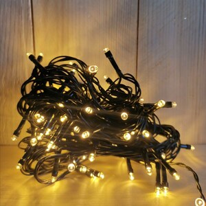 Könnte beinhalten: Ein Knäuel schwarzer Lichterketten mit warmweißen LED-Lampen. Die Lichter sind zusammengerollt und bereit zum Aufhängen zur Dekoration.