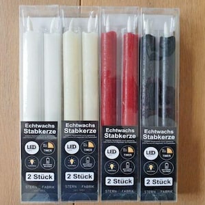 Könnte beinhalten: Vier Sets LED-Spitzkerzen in Klarsichtverpackung. Die Kerzen sind weiß, cremefarben, rot und schwarz. Jede Packung trägt die Aufschrift "Echtwachs Stabkerze" und "2 Stück".