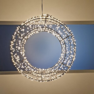 Könnte beinhalten: Eine kreisförmige Hängeleuchte mit einem Metallrahmen, der mit zahlreichen kleinen, hellweißen LED-Lichtern verziert ist. Die Struktur besteht aus zwei konzentrischen Ringen, die durch dünne Drähte verbunden sind und einen Sterneneffekt erzeugen.