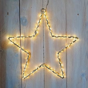 Könnte beinhalten: Eine sternförmige Leuchtdekoration. Der Stern besteht aus silberfarbenem, gedrehtem Draht und wird von warmweißen LED-Leuchten beleuchtet. Er hängt an einem kleinen Metallring und einem transparenten Draht, ideal für festliche Anlässe.