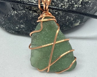 White sea glass pendant wrapped with anti tarnish rose gold plated wire on a black cord chain.
