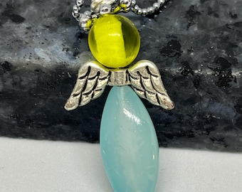 May include: A silver-toned angel pendant necklace. The pendant features a yellow bead head, silver wings, and a light blue teardrop-shaped body. The necklace has a delicate silver chain.