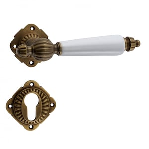 May include: A set of antique brass door handles with a white ceramic lever. The handles have a decorative design and a keyhole.