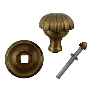 Könnte beinhalten: Messing-Türknopf mit einem geriffelten, pilzförmigen Griff, einer runden Grundplatte mit einem quadratischen Schlüsselloch und einer Schraube mit Unterlegscheibe und Mutter.