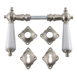 Puede incluir: Un juego de dos manillas de puerta de porcelana blanca con herrajes niquelados. Las manillas tienen un diseño tradicional con un pomo redondo y un eje largo y cónico. El juego incluye dos manillas, dos rosetas y dos tapas para los agujeros de las llaves.