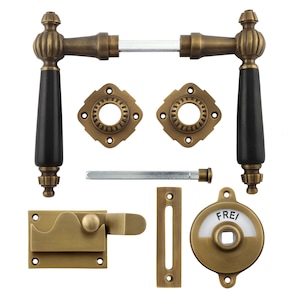 May include: A set of antique brass door hardware with black wooden handles. The set includes two door knobs, a latch, a strike plate, a door handle, and a keyhole cover with the word "FREI" on it.