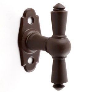 May include: A brown metal window latch with a T-shaped handle and a decorative plate. The handle has a pointed top and bottom.
