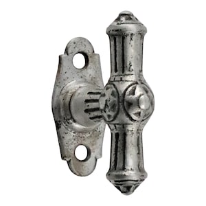 May include: A silver-toned metal window latch with a decorative design. The latch has a T-shaped handle with a rounded top and a rectangular base. The handle is attached to a plate with two holes for mounting.