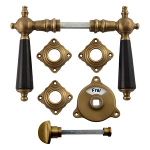 May include: Brass door hardware set with black handles, two round escutcheons, a square escutcheon, and a round escutcheon with the word "Frei" on it.