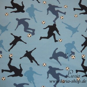 May include: A blue fabric with a repeating pattern of black silhouettes of soccer players kicking a ball. The fabric has a light blue background with white soccer balls scattered throughout.