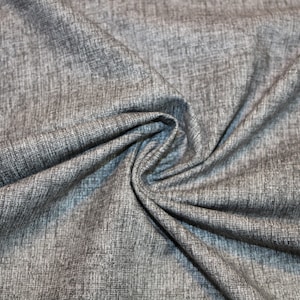 Può includere: Primo piano di un tessuto grigio testurizzato con un sottile motivo intrecciato. Il tessuto è piegato e drappeggiato, mostrando la sua texture morbida e fluida.