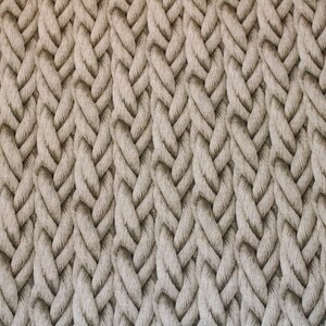 Könnte beinhalten: Nahaufnahme eines beigefarbenen Strickstoffes mit einem strukturierten, geflochtenen Muster.