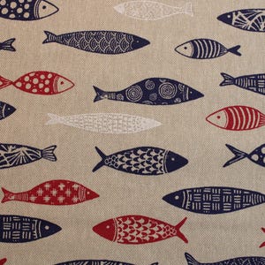 Op de afbeelding: Een beige stof met een herhalend patroon van blauwe en rode vissen. De vissen hebben verschillende ontwerpen, waaronder swirls, stippen en lijnen.