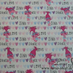 Könnte beinhalten: Weißer Stoff mit einem sich wiederholenden Muster aus rosa und blauen Herzen, rosa und blauem Text und Comicbildern von pinkhaarigen Trollen mit blauen Augen. Der Text lautet "Love", "Sing" und "Dance".