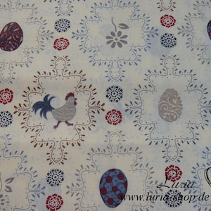 Op de afbeelding: Witte stof met een herhalend patroon van blauwe en bruine gestileerde eieren, rode bloemen en een haan. De stof heeft ook een grijze bloem en een grijs gestileerd ei. De tekst "Luria www.luria-shop.de" is afgedrukt in de rechterbenedenhoek.