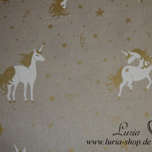 Op de afbeelding: Beige stof met een wit eenhoornpatroon en gouden glittersterren. De stof heeft de tekst "Luria www.luria-shop.de" in de rechterbenedenhoek.