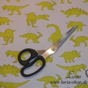 May include: A white fabric with a repeating pattern of yellow dinosaurs. A pair of silver scissors is lying on top of the fabric. The text "Luria www.luria-shop.de" is printed on the fabric.
