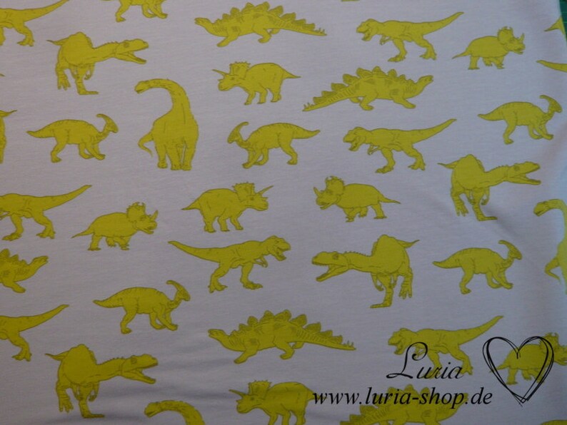 May include: White fabric with a repeating pattern of yellow dinosaurs. The dinosaurs are in various poses and sizes. The fabric has a subtle texture.
