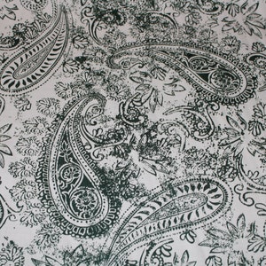 May include: A white fabric with a dark green paisley pattern. The pattern is a traditional paisley design with intricate details.