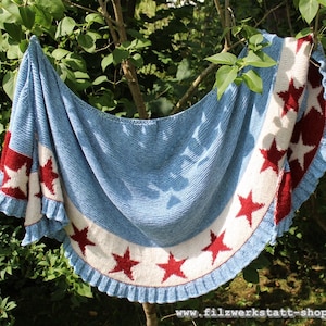 May include: A blue knitted shawl with a white and red star pattern around the edge. The shawl is hanging on a tree branch.