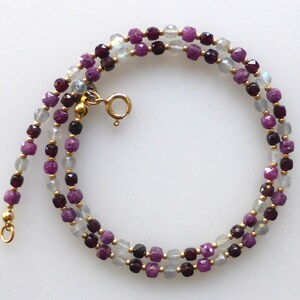 Könnte beinhalten: Eine zarte goldene Kettenkette mit abwechselnden facettierten Perlen aus klaren, violetten und dunkelroten Edelsteinen.
