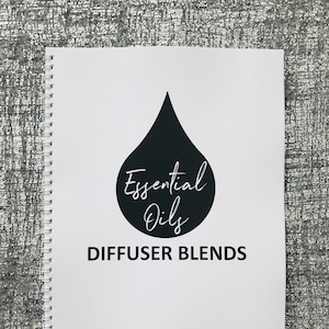 Könnte beinhalten: Ein weißes spiralgebundenes Notizbuch mit einer schwarzen Wassertropfengrafik und dem Text "Essential Oils Diffuser Blends".