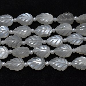 May include: Strands of white, leaf-shaped beads with detailed veining. The beads are strung together with small, round white beads, creating a delicate and elegant design. The beads are likely made of a pearlescent material, giving them a subtle sheen.